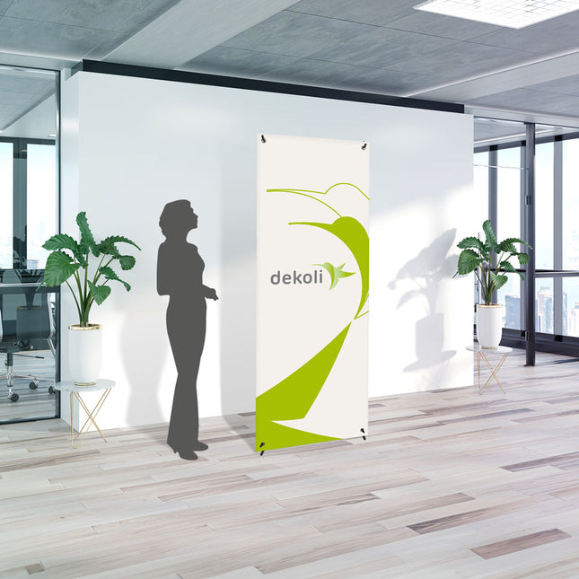 Bannerdisplay Easy X mit Banner zum Aufhängen mit  Modell zum Größenvergleich. Unser Modell ist 165cm groß und ist in einem Büro. Das weiße und grüne Dekoli Logo wird farbintensiv gedruckt.