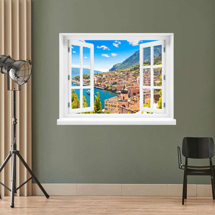 Selbstklebendes Wandtattoo an einer olivgrünen Studiowand, geformt wie ein offenes Fenster, präsentiert die idyllische Aussicht auf dieses berühmte Dorf am See, umgeben von Bergen und strahlendem Sonnenschein. 