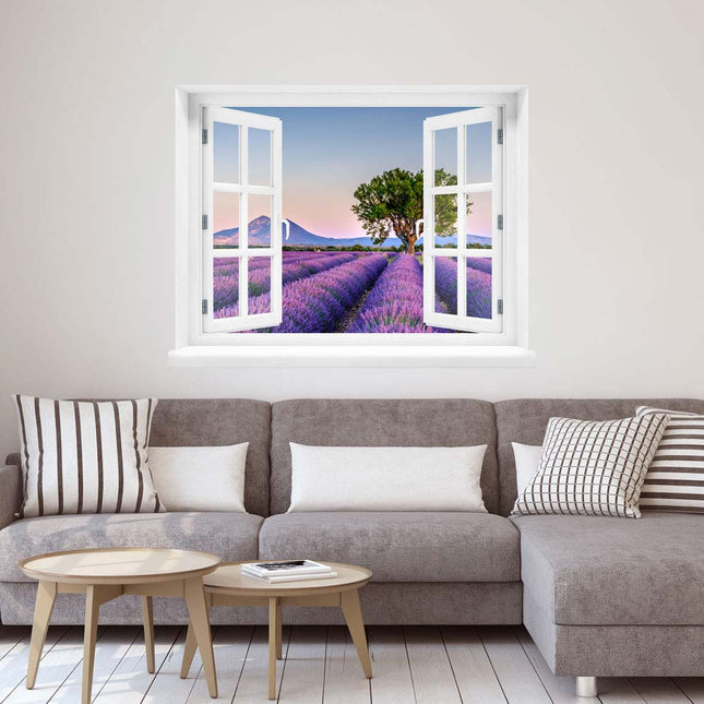Genießen Sie den Charme der Provence in Ihrem Zuhause! Selbstklebendes Wandbild, in Form eines geöffneten Fensters mit einem weißen Rahmen, mit träumerischer Aussicht auf ein Lavendelfeld mit Bergen im Hintergrund in sommerlichem Abendlicht. Platziert über einer Couch, die perfekte Dekoration für Ihre Auszeit daheim.