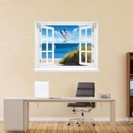 Erleben Sie die Ruhe des Strandes in Ihrem eigenen Zuhause! Selbstklebendes Wandbild in Form eines geöffneten Fensters mit Ausblick auf einen Strand, strahlend blaues Wasser und zwei fliegenden Möwen, als Deko an einer Wand hinter einem Schreibtisch.