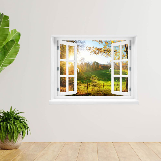 Bringen Sie die Schönheit der Herbstlandschaft zu sich nach Hause! Selbstklebendes Wandbild eines geöffneten Fensters mit Ausblick auf eine herbstliche, grüne Waldlichtung und Sonnenstrahlen, als Dekoration an einer Wand mit Pflanzen daneben.